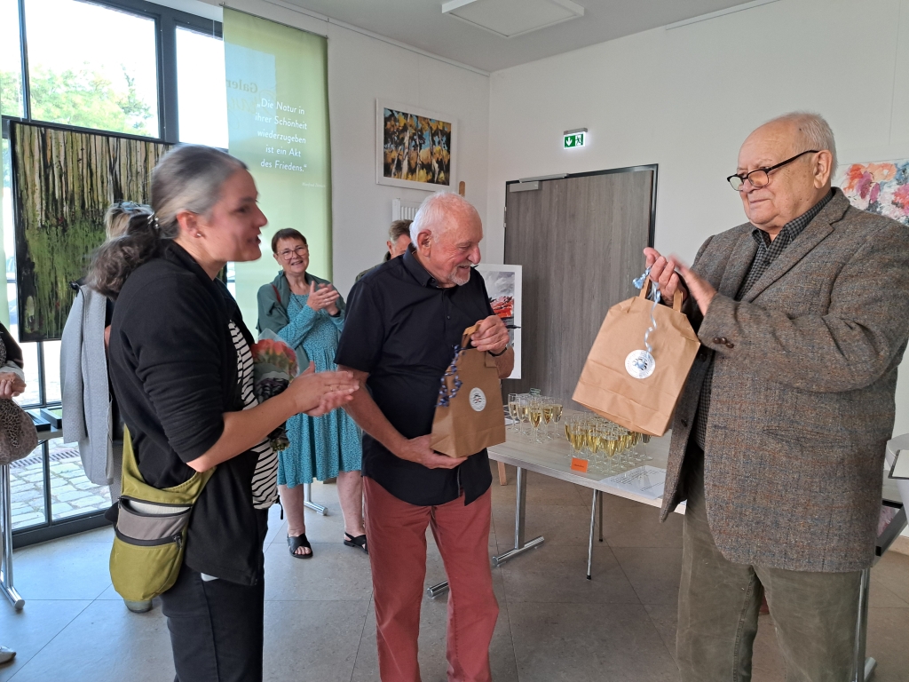 Ein Tütchen mit Inhalt: Svenja Kauer von der Schlossgut-GmbH begrüßt damit Aussteller Manfred Zémsch und Laudator Gerd Hünger (v. l.).